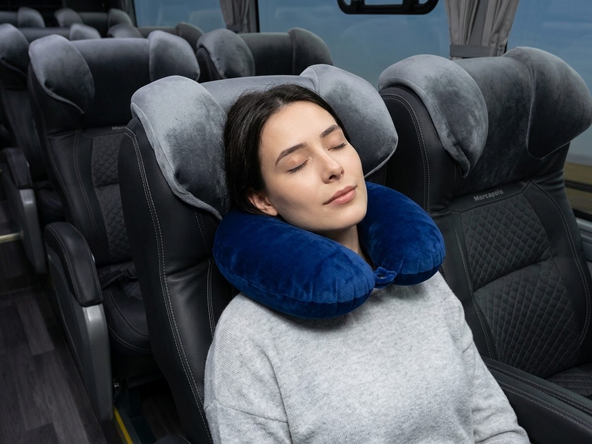 Passageira usando travesseiro de pescoço em poltrona de ônibus rodoviário